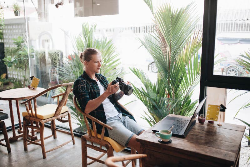 Creatieve fotograaf die professionele camera houden, die bij koffie met laptop zitten stock foto's Creatieve fotograaf die professionele camera houden, die bij koffie met laptop zitten stock foto's