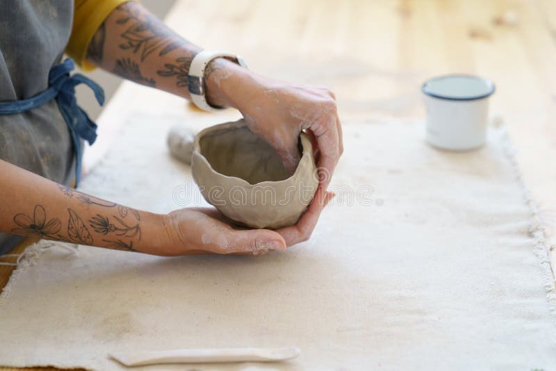 Creating pottery: table in ceramic studio with master hands shaping clay pot. Woman potter sculpting