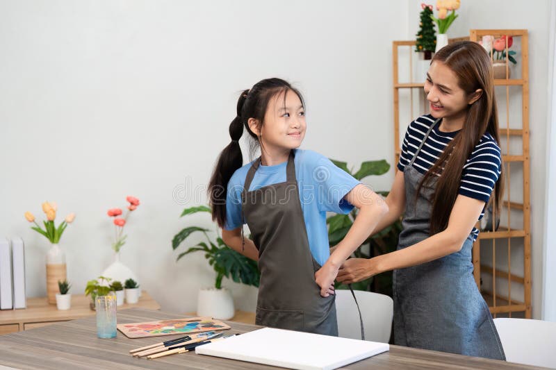Creative bonding through art: Mother helping daughter wear an apron stock images