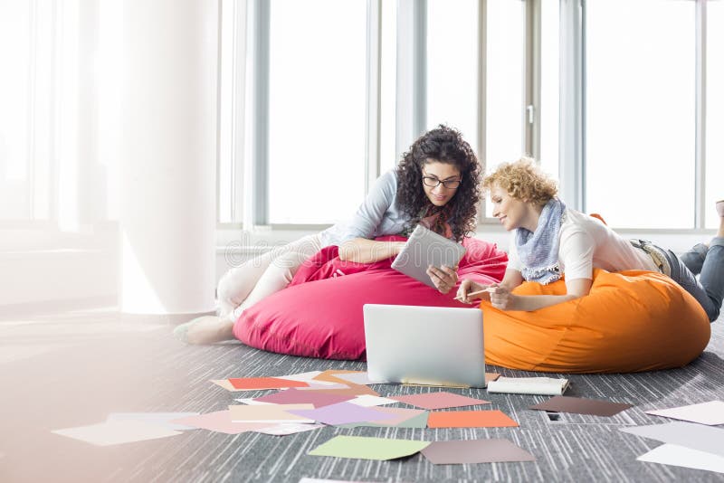 Creative businesswomen using tablet PC while relaxing on beanbag chairs at office