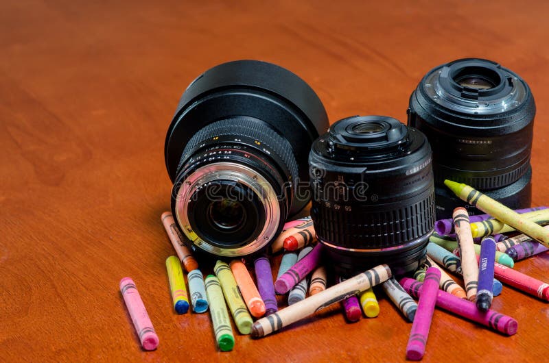 Three camera lenses one with plastic mount and the others metal on top of colorful crayons. Three camera lenses one with plastic mount and the others metal on top of colorful crayons