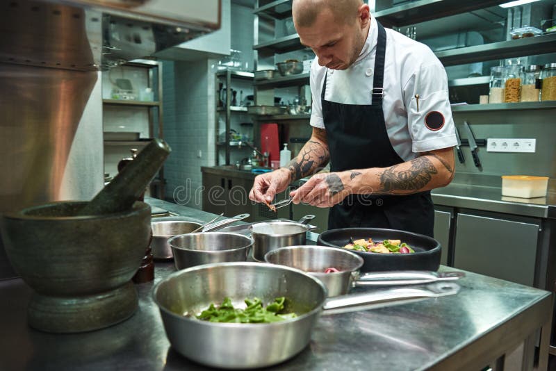 Creative cooking. Confident chef with several tattoos on his arms garnishing italian pasta in a restaurant kitchen stock images Creative cooking. Confident chef with several tattoos on his arms garnishing italian pasta in a restaurant kitchen stock images