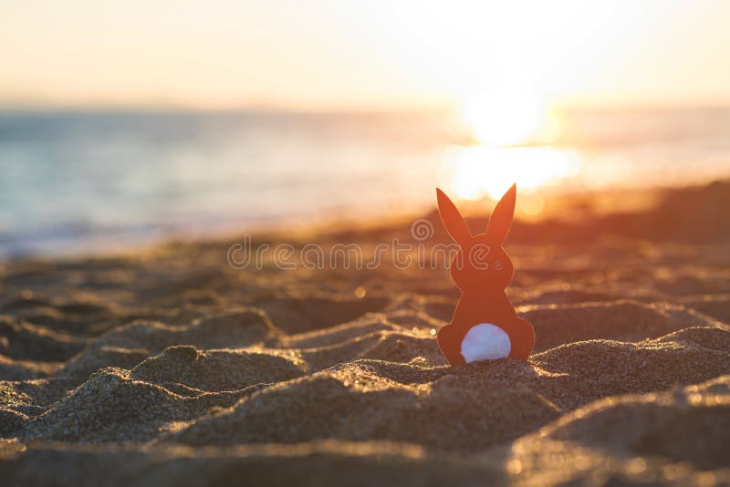 Creative easter concept photo of red paper bunny on the sand on the beach at sunset. Concept. royalty free stock images