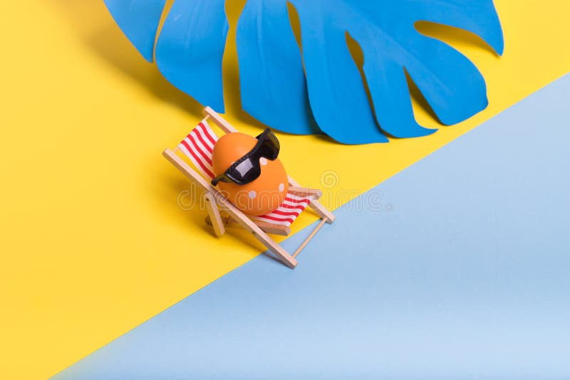 Creative funny composition with Easter egg with sunglasses while sitting on deck chair on illuminating yellow and pastel blue royalty free stock photos