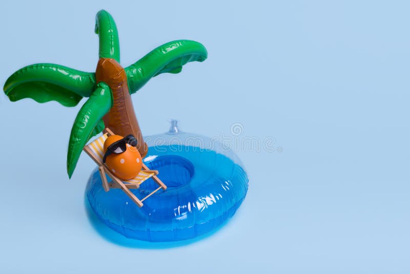 Creative funny composition with Easter egg with sunglasses while sitting on deck chair on inflatable palm tree stock photography