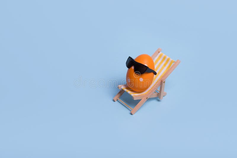 Creative funny composition with Easter egg with sunglasses while sitting on deck chair on pastel blue background stock photos