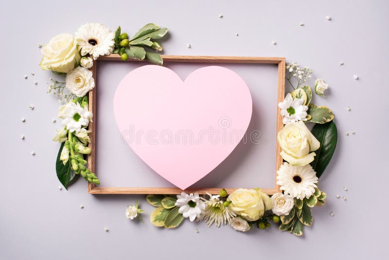 Creative layout with pink flowers, paper heart over grey background. Top view, flat lay. Spring, summer or garden concept. Present stock photography