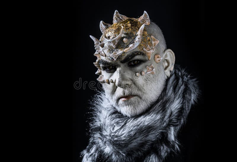 Demonic creature with thorns on head isolated on black background. King of realm of perpetual cold. Man with fictional make-up and white beard wearing fur collar. Demonic creature with thorns on head isolated on black background. King of realm of perpetual cold. Man with fictional make-up and white beard wearing fur collar.