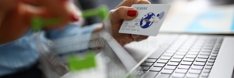 Credit bank card is holding small shopping basket next to laptop.