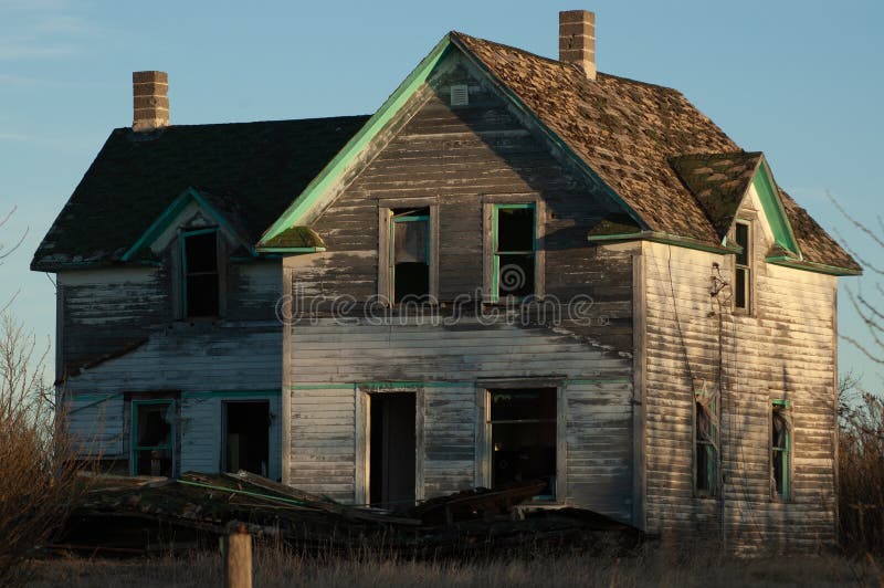 Creepy, old and aged abandoned wooden house in a field under the blue sky