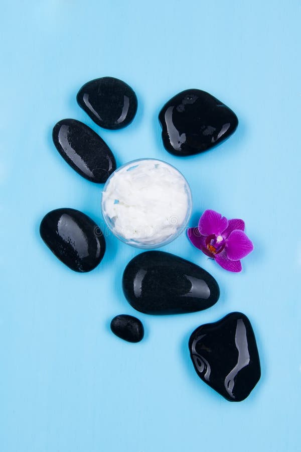 Crema con el olor de las orquídeas rodeadas por las piedras negras en un azul foto de archivo Crema con el olor de las orquídeas rodeadas por las piedras negras en un azul foto de archivo