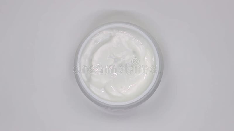 Crema cosmética blanca en un frasco rota sobre un fondo blanco