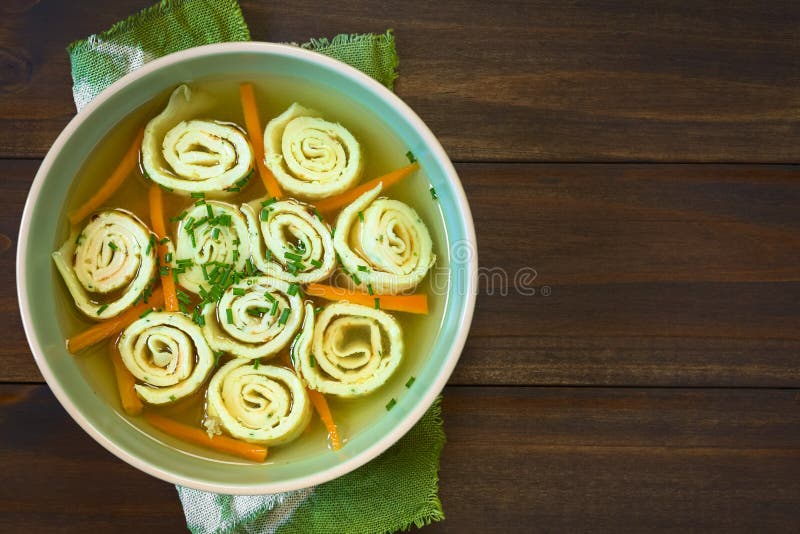 Traditional German Flaedlesuppe and Austrian Frittatensuppe based on consomme with rolls or stripes of pancake or crepe garnished with chives, photographed overhead on wood with natural light Selective Focus, Focus on the soup. Traditional German Flaedlesuppe and Austrian Frittatensuppe based on consomme with rolls or stripes of pancake or crepe garnished with chives, photographed overhead on wood with natural light Selective Focus, Focus on the soup