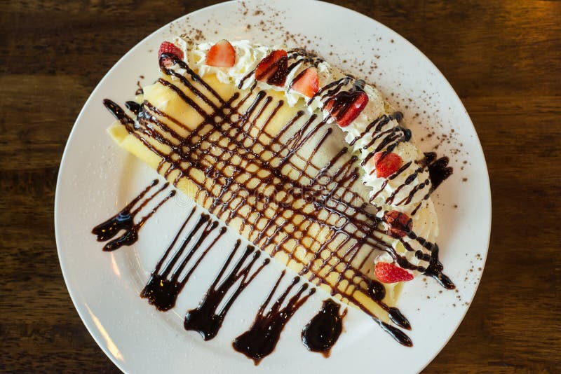 Crepes con los plátanos y la salsa del caramelo del chocolate, rematando con crema del azote y la fresa en la tabla fotografía de archivo Crepes con los plátanos y la salsa del caramelo del chocolate, rematando con crema del azote y la fresa en la tabla fotografía de archivo