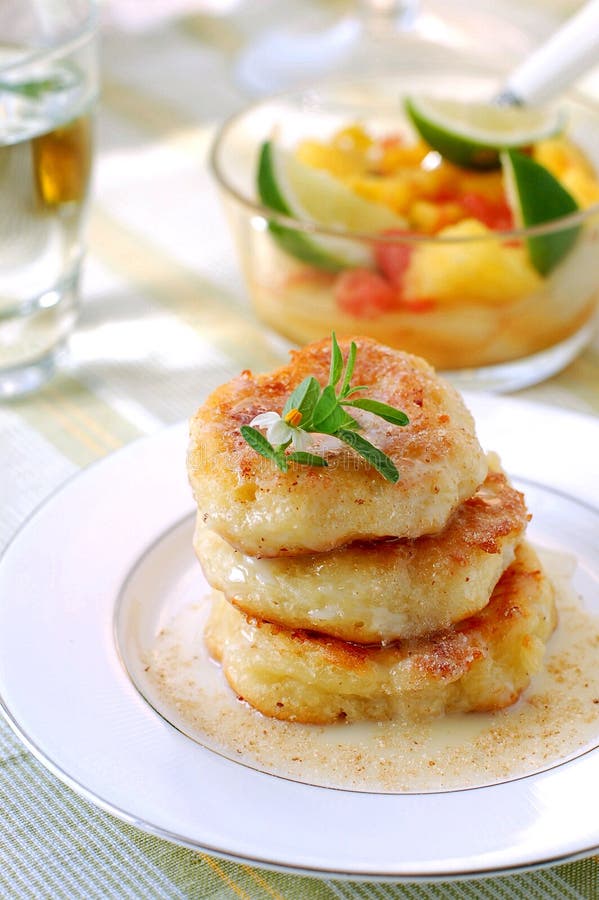 A tower of curd pancakes covered with a cream and a bowl of fruit salad as a background. A tower of curd pancakes covered with a cream and a bowl of fruit salad as a background.