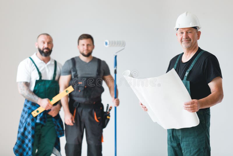 Three professional builder with painting roll and renovation plans standing in empty interior royalty free stock photos