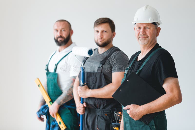 Three professional builder wearing overalls standing in empty interior stock image