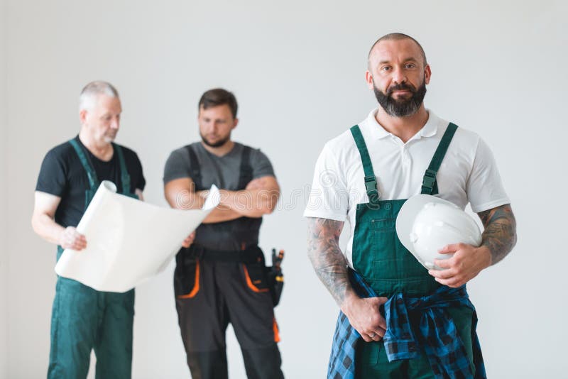 Three professional builder wearing overalls standing in empty interior royalty free stock image