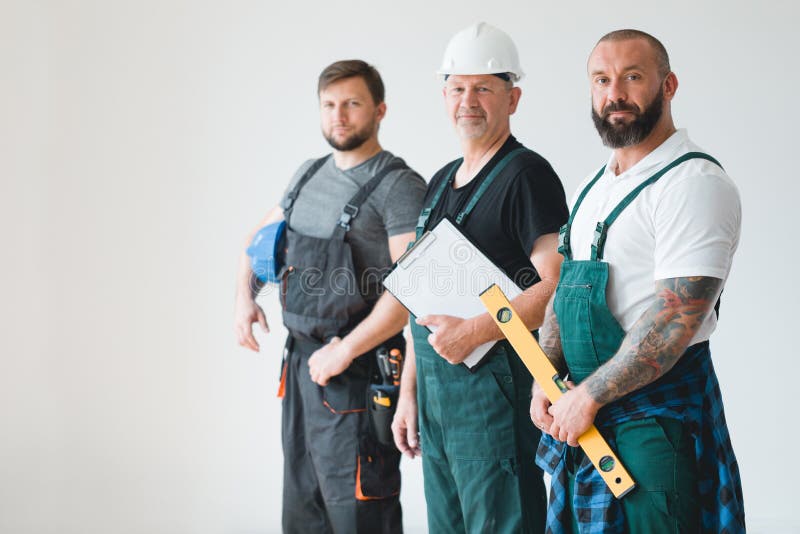 Three professional builder wearing overalls standing in empty interior stock images