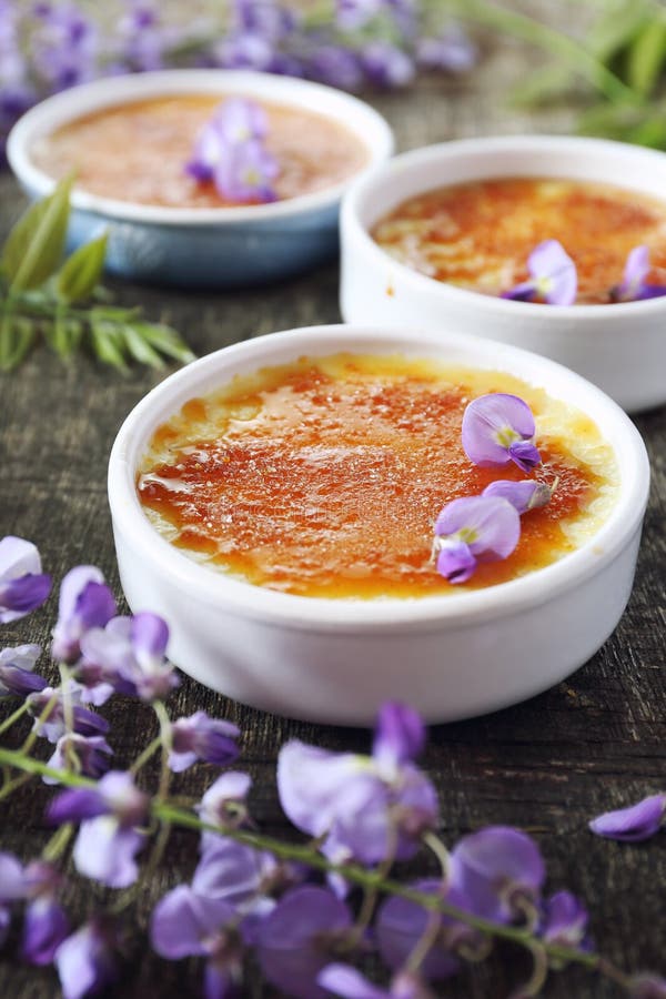 Creme brulee, french traditional dessert, three portions, flowering purple wisteria dressing. Rustic style. Creme brulee, french traditional dessert, three portions, flowering purple wisteria dressing. Rustic style
