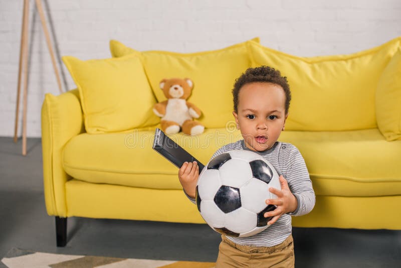 criança afro-americano adorável que guardam a bola de futebol e controlador remoto imagem de stock criança afro-americano adorável que guardam a bola de futebol e controlador remoto imagem de stock