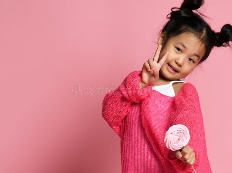 A criança asiática nova feliz da menina lambe come doces doces grandes felizes do lollypop no rosa