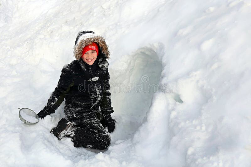 A criança bonito empacotada toda acima para o inverno está construindo um túnel em uma pilha da neve