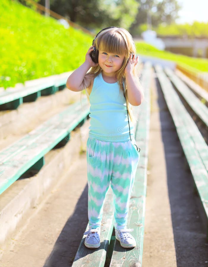 A criança da menina escuta a música nos fones de ouvido fotografia de stock A criança da menina escuta a música nos fones de ouvido fotografia de stock