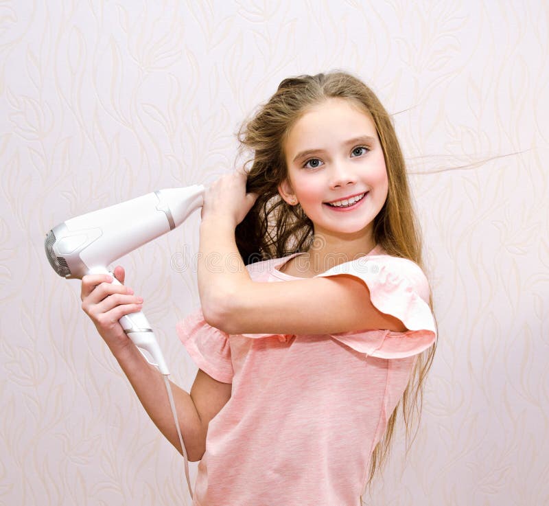 Criança de sorriso bonito da menina que seca seu cabelo longo com secador de cabelo imagens de stock royalty free Criança de sorriso bonito da menina que seca seu cabelo longo com secador de cabelo imagens de stock royalty free