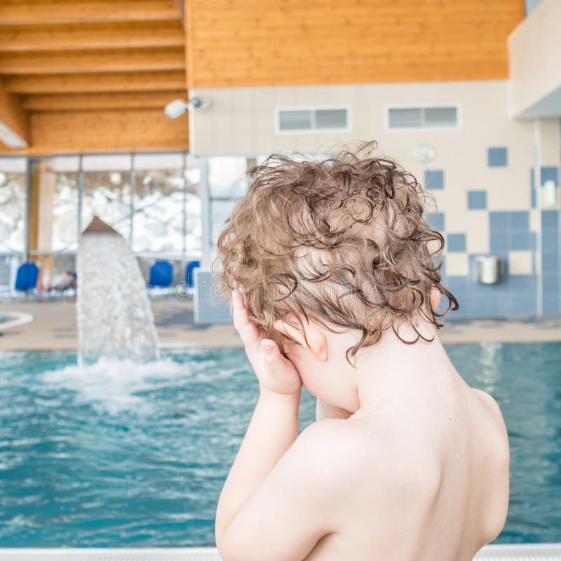 A criança está escondendo seus olhos com suas mãos ao lado de uma piscina imagens de stock royalty free A criança está escondendo seus olhos com suas mãos ao lado de uma piscina imagens de stock royalty free