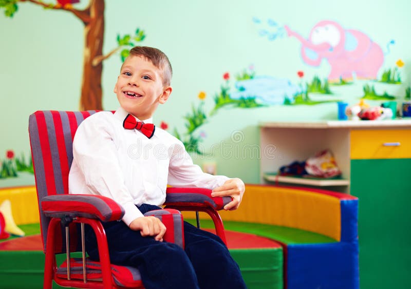Criança feliz bonito na cadeira de rodas, panos contentes vestindo no centro para crianças com necessidades especiais