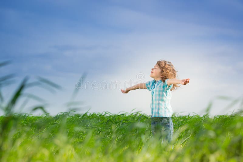 Happy kid with raised arms in green spring field against blue sky. Freedom and happiness concept. Happy kid with raised arms in green spring field against blue sky. Freedom and happiness concept