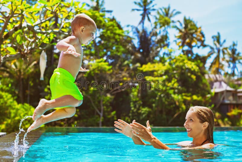 A criança feliz salta para serir de mãe às mãos na piscina fotografia de stock royalty free A criança feliz salta para serir de mãe às mãos na piscina fotografia de stock royalty free