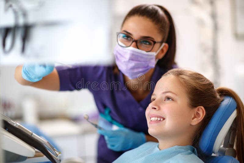Criança na cadeira dental com o dentista fêmea que olha o pé dental