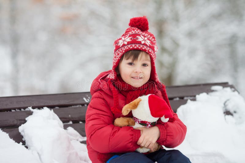 Criança pequena adorável, menino, jogando em um parque nevado, guardando ted fotos de stock Criança pequena adorável, menino, jogando em um parque nevado, guardando ted fotos de stock