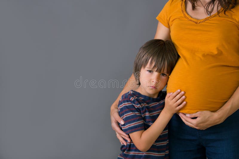 Criança pequena, menino, abraçando sua mãe grávida em casa, isolado imagem de stock Criança pequena, menino, abraçando sua mãe grávida em casa, isolado imagem de stock