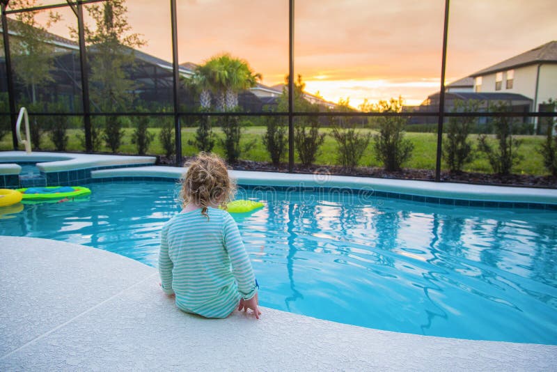 Criança que senta-se na borda de uma piscina em um dia de verão morno