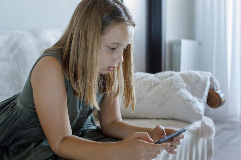 Criança a usar telemóvel em casa. Pequeno(a) a jogar um videojogo no quarto imagem de stock