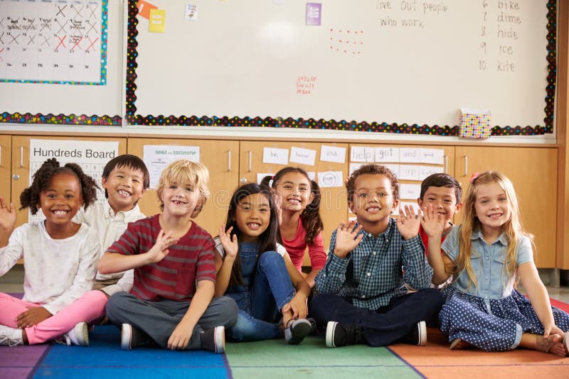 Crianças da escola primária que sentam-se no assoalho da sala de aula