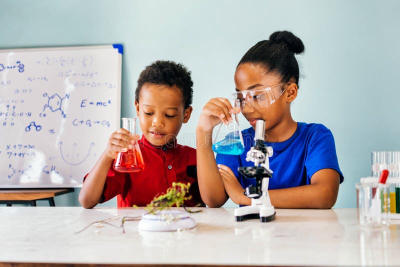 Cheerful black pretty smart children in casual clothes sitting in school chemistry laboratory and holding flasks with colourful liquids. Cheerful black pretty smart children in casual clothes sitting in school chemistry laboratory and holding flasks with colourful liquids