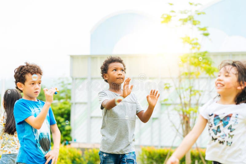 Crianças felizes que fundem bolhas de sabão no parque do verão Criança e amigos no jogo pré-escolar internacional uma bolha imagem de stock royalty free Crianças felizes que fundem bolhas de sabão no parque do verão Criança e amigos no jogo pré-escolar internacional uma bolha imagem de stock royalty free