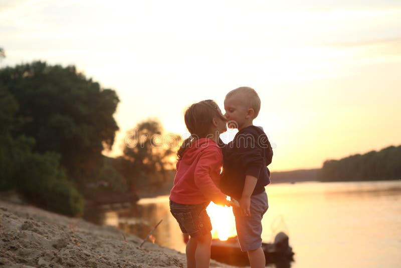 Crianças menino e rio do por do sol do beijo da menina foto de stock Crianças menino e rio do por do sol do beijo da menina foto de stock
