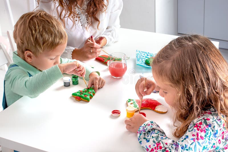 Crianças pequenas com uma babá para se preparar para o Natal Eles sentam-se à mesa na sala fotos de stock Crianças pequenas com uma babá para se preparar para o Natal Eles sentam-se à mesa na sala fotos de stock