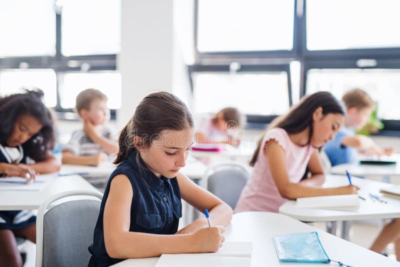 Crianças pequenas concentradas sentadas na escrivaninha na sala de aula, escrevendo