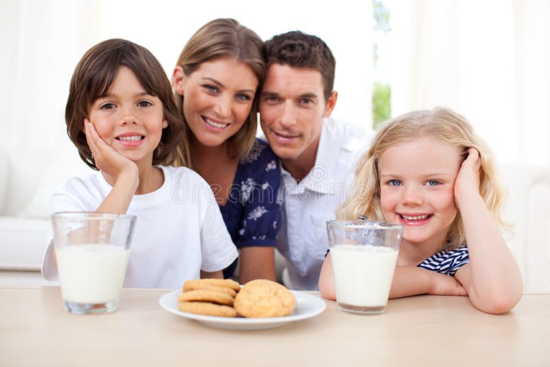 Children eating biscuits and drinking milk with their parents in the kitchen. Children eating biscuits and drinking milk with their parents in the kitchen