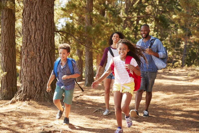 Crianças que correm antes de pais na família que caminha a aventura