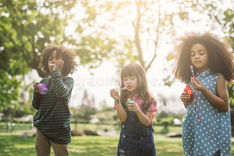 Crianças a brincar a soprar bolhas juntas no campo fotografia de stock