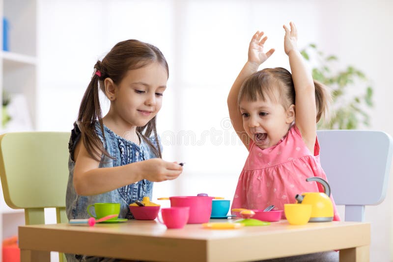 Crianças que jogam com utensílios de mesa plásticos