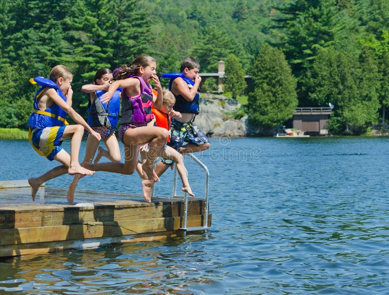 Crianças que têm o divertimento do verão que salta fora da doca no lago