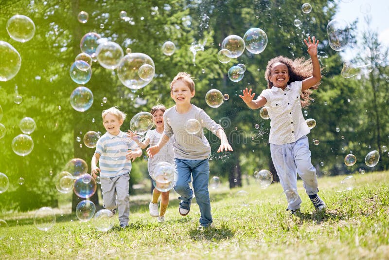 Multi-ethnic group of little friends with toothy smiles on their faces enjoying warm sunny day while participating in soap bubbles show. Multi-ethnic group of little friends with toothy smiles on their faces enjoying warm sunny day while participating in soap bubbles show